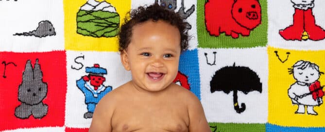 a laughing little boy in red bloomers in front of a personalised blanket