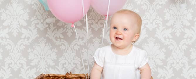 a little girl in a giant wicker basket with a bunch of balloons floating above it
