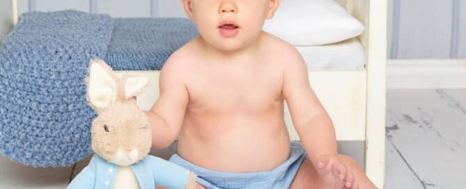 a little boy poses with a Peter Rabbit toy in front of a white bed