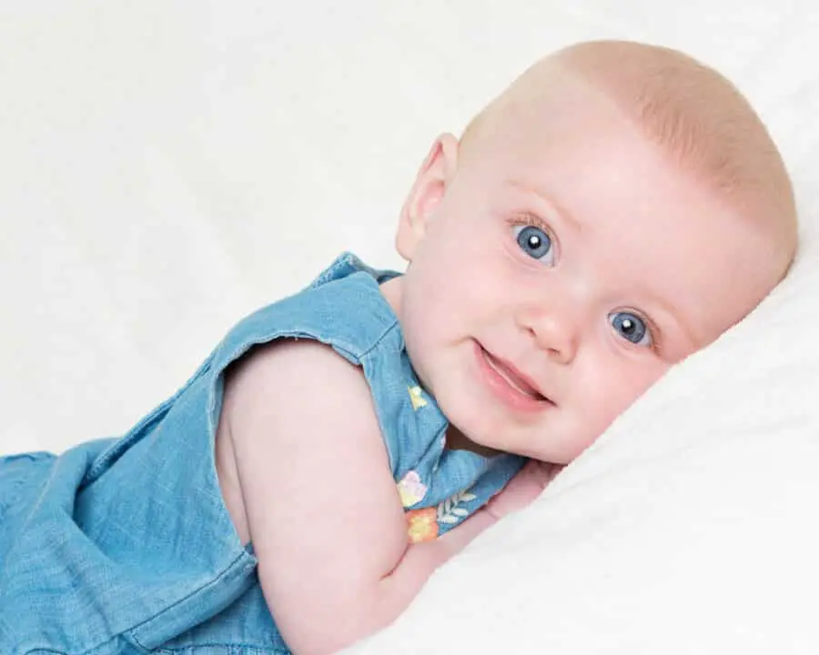 a bright blue eyed girl looks into the camera lying on her tummy