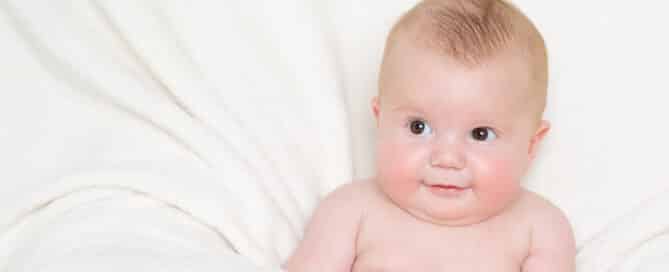 a little boy sits wrapped in a cream blanket like a nest