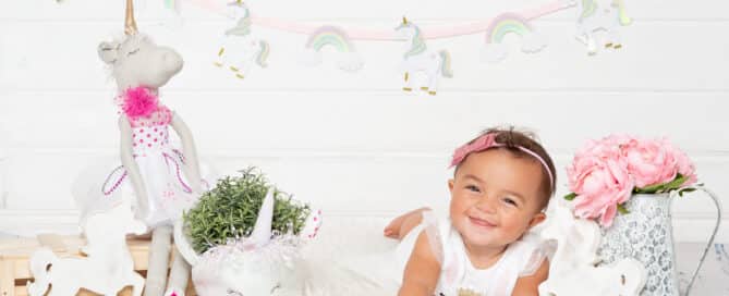 a little girl poses on her tummy with unicorn props