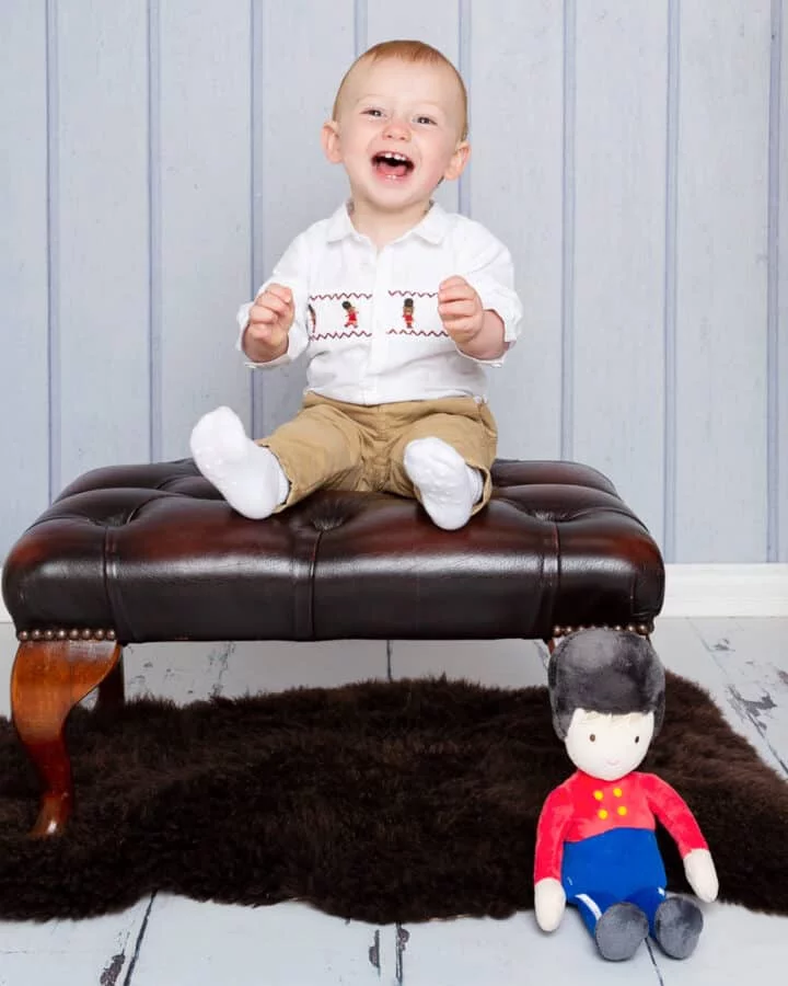 a little boy sits on a stool laughing with his favourite guardsman toy