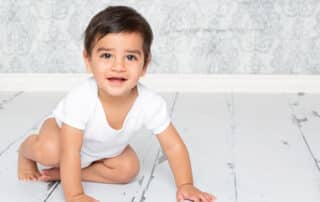 a little boy in a white vest photographed against a blue damask background
