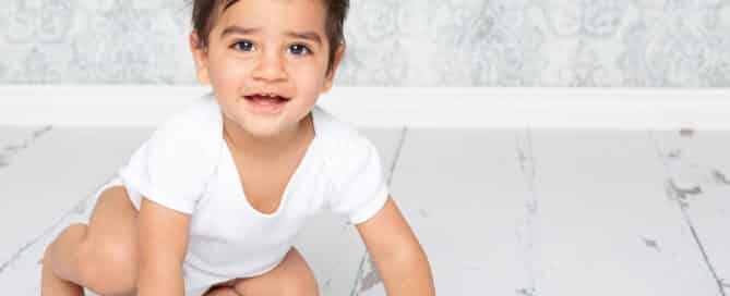 a little boy in a white vest photographed against a blue damask background