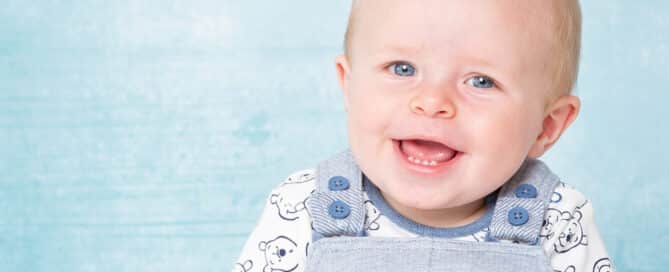 a blue eyed baby boy smiles for the camera against a matching blue background