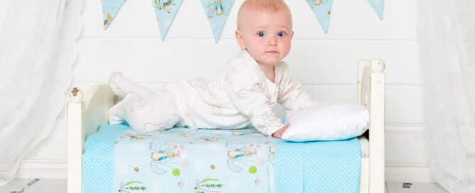 a little baby on a miniature white bed with Peter Rabbit themed quilt and bunting