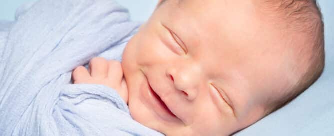 A smiling newborn wrapped in blue and lying on a blue blanket asleep
