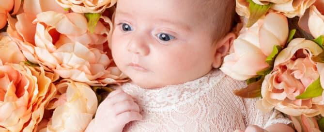 a little girl in a peach outfit poses in a bed of peach peony flowers