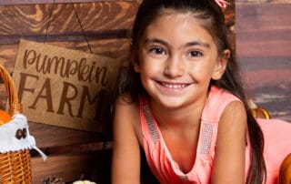 a little girl poses with a pumpkin at a pumpkin patch themed photo shoot