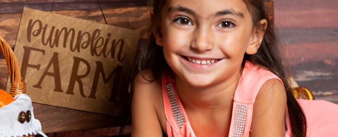 a little girl poses with a pumpkin at a pumpkin patch themed photo shoot