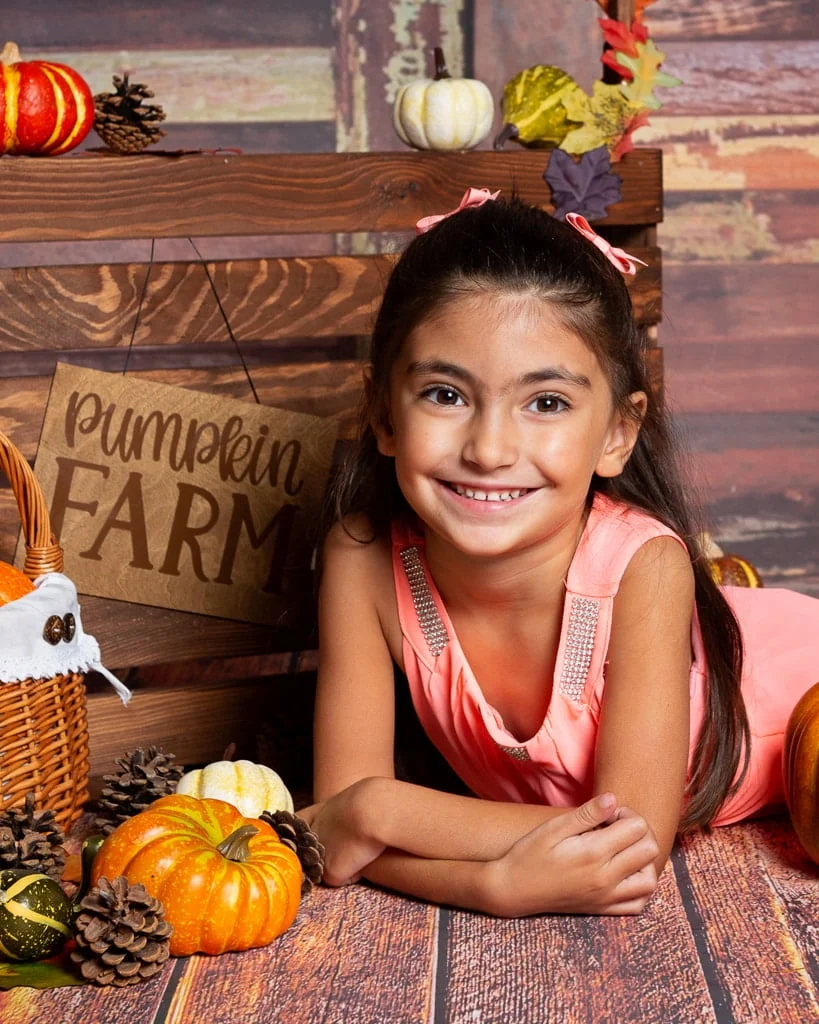 a little girl poses with a pumpkin at a pumpkin patch themed photo shoot