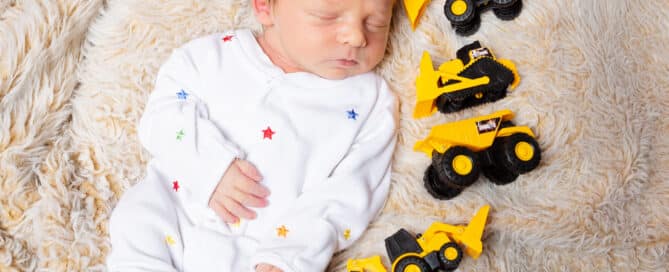a sleeping newborn surrounding by digger toys
