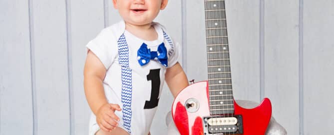 a baby boy poses in the studio next to his dad's guitar