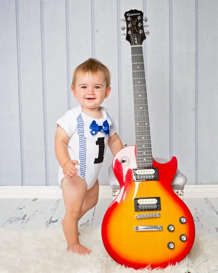 Baby Photography East Grinstead West Sussex a little boy stands next to his dad's guitar at a professional baby photo shoot
