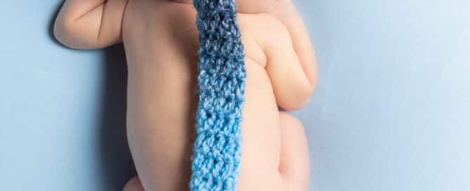 A newborn baby viewed from the top while lying on their tummy wearing a long tailed blue hat