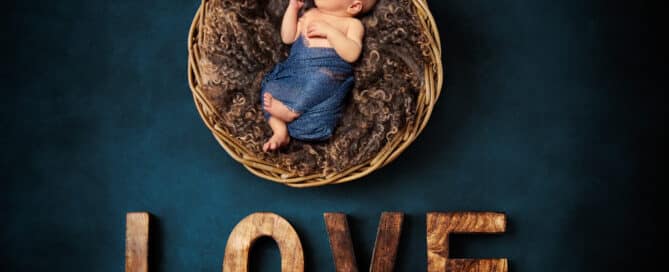 a digitally composited newborn image of a sleeping newborn in a wood bowl against a teal backdrop