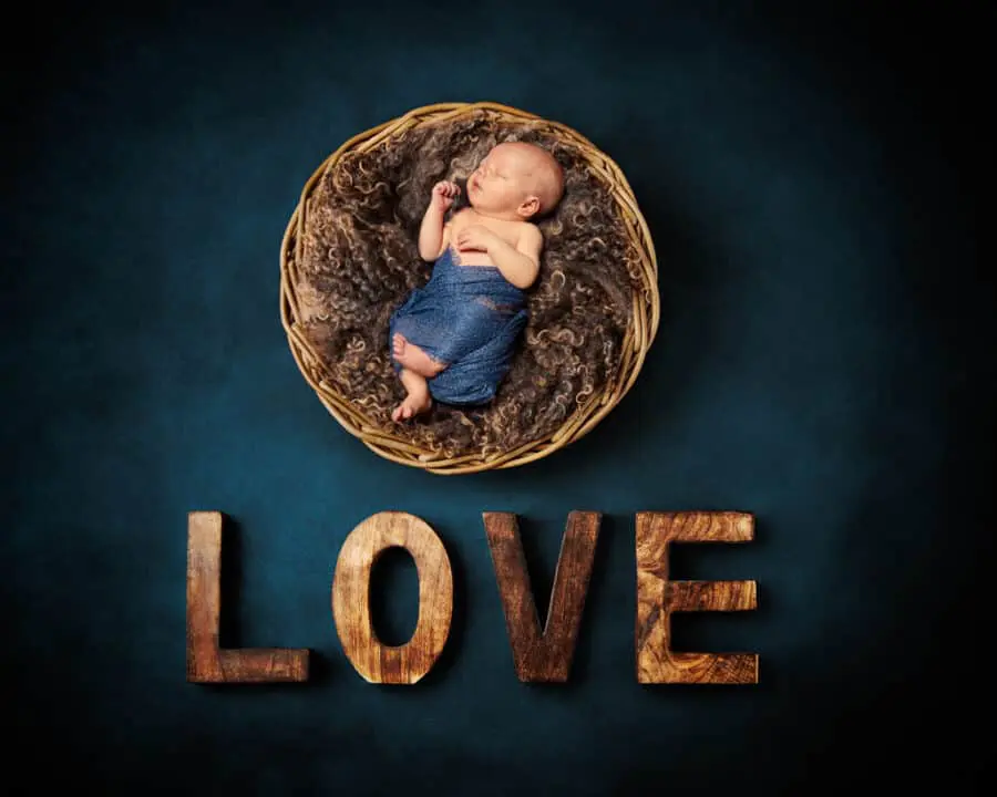 a digitally composited newborn image of a sleeping newborn in a wood bowl against a teal backdrop