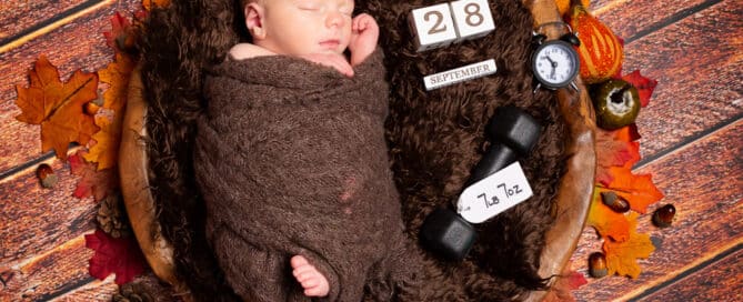 a newborn sleeps in a wooden bowl surrounding by autumn leaves