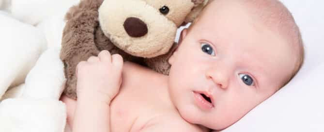 a newborn baby with their eyes open and looking at the camera while cuddling a stuff monkey