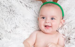a smiling baby in a fluffy blanket and wearing reindeer antlers in a Christmas themed photo