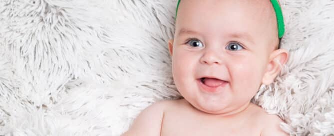a smiling baby in a fluffy blanket and wearing reindeer antlers in a Christmas themed photo