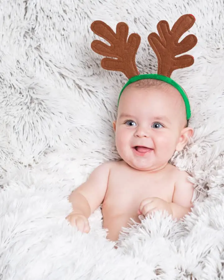 Baby Photography East Grinstead West Sussex a smiling baby in a fluffy blanket and wearing reindeer antlers in a Christmas themed photo