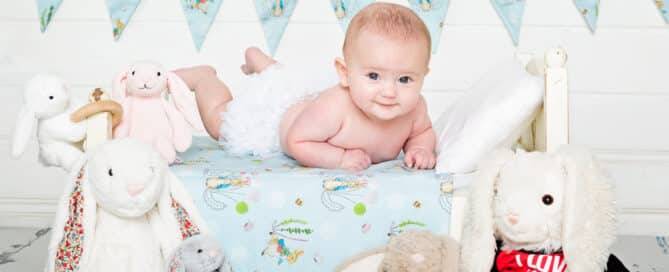 a little baby on a bed with a lot of rabbit toys
