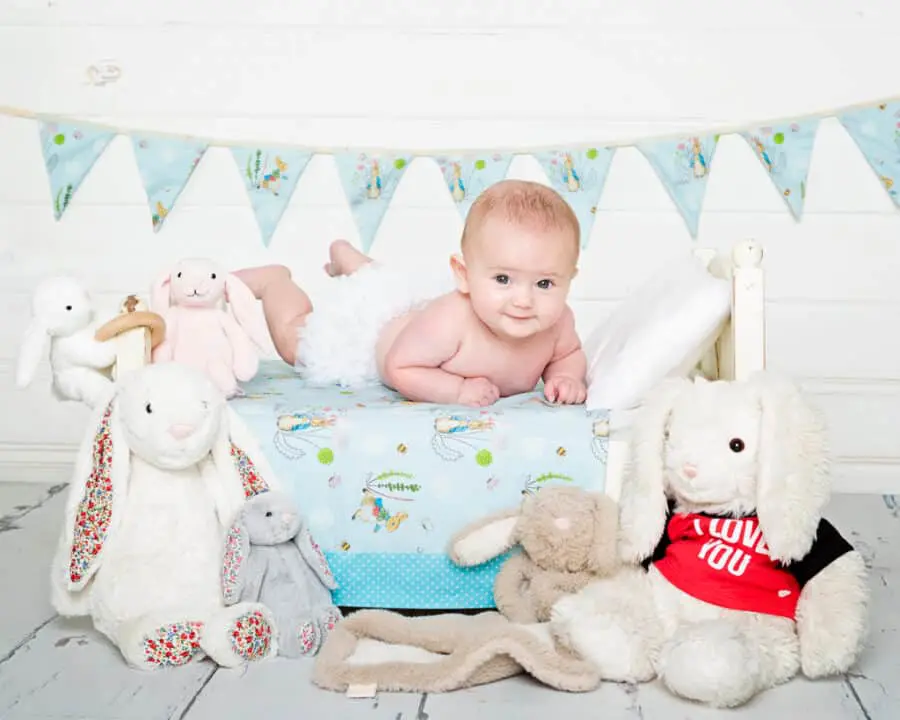 a little baby on a bed with a lot of rabbit toys