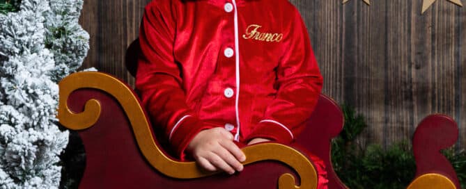a little boy in christmas pjs sits in a mini sleigh at a festive photo shoot