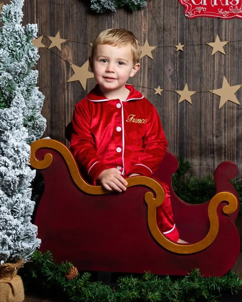 a little boy in christmas pjs sits in a mini sleigh at a festive photo shoot