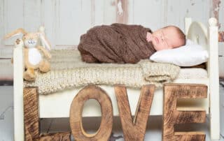 a newborn baby on a white bed with neutral tones blankets and wooden letters spelling LOVE