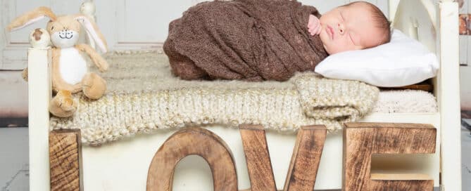 a newborn baby on a white bed with neutral tones blankets and wooden letters spelling LOVE