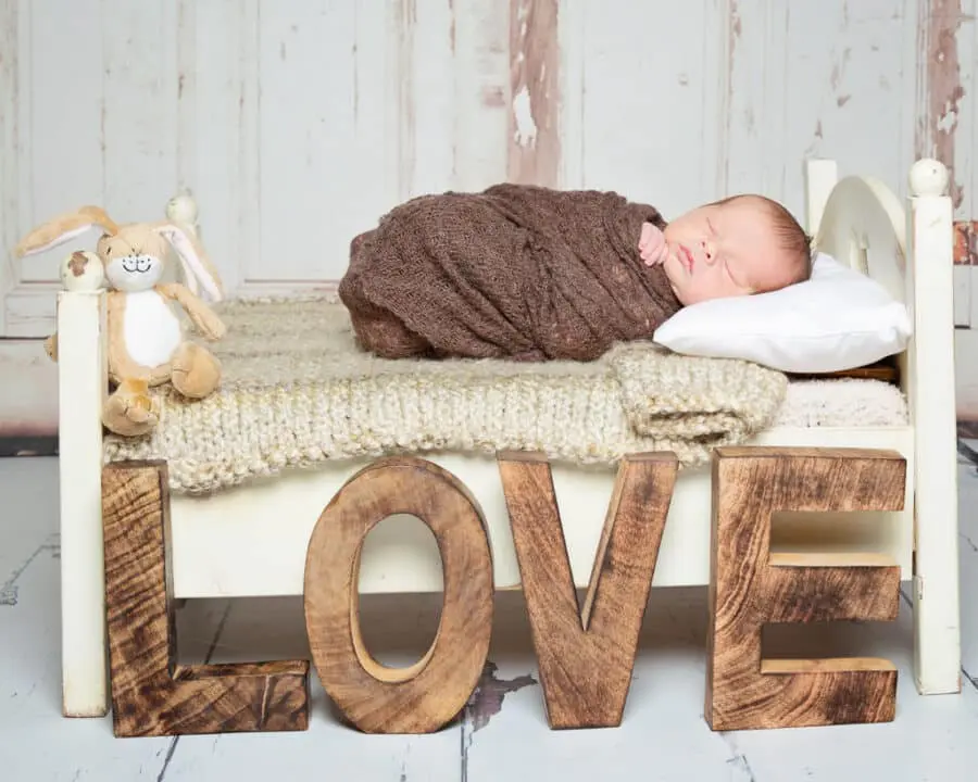 a newborn baby on a white bed with neutral tones blankets and wooden letters spelling LOVE