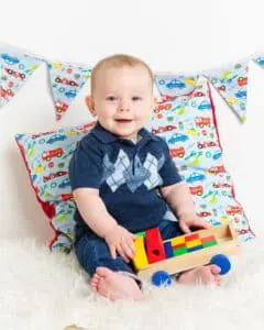 Baby Photography East Grinstead West Sussex a little boy is holding a wooden truck and posing for his photo at a professional photo shoot