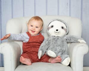 a little boy sitting on a grey chair with this favourite soft sloth toy