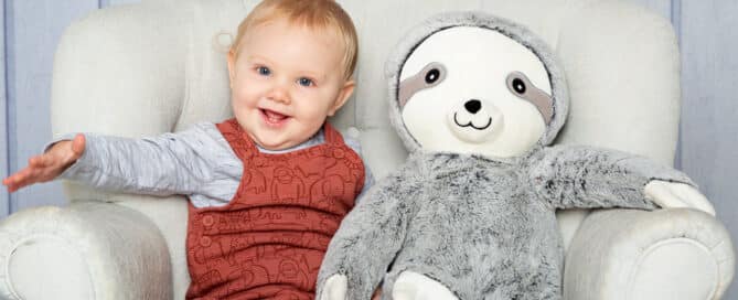 a little boy sitting on a grey chair with this favourite soft sloth toy