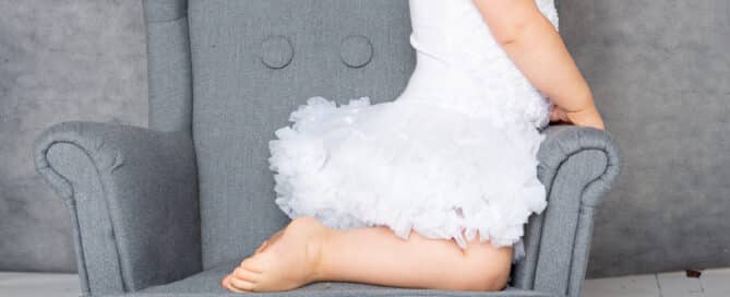 a little girl on a mini wingback chair in a white dress at a photo shoot