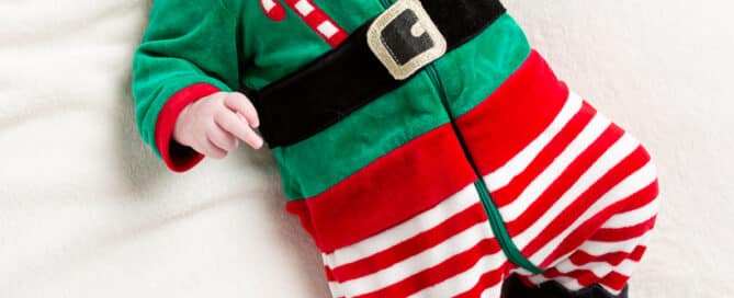 a small baby lies on a white blanket wearing an elf costume