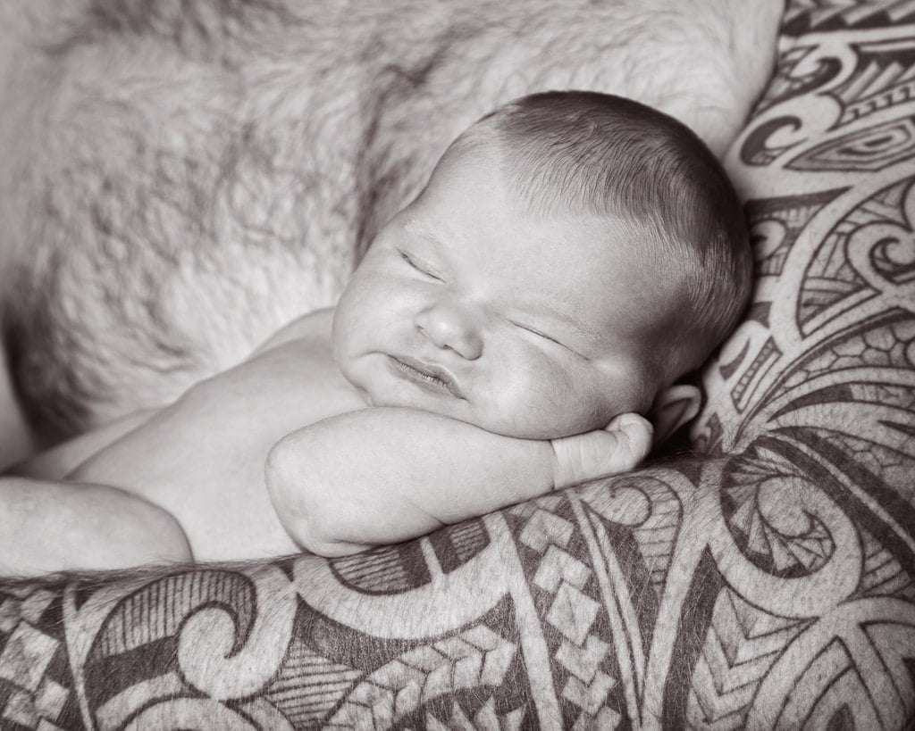 a little baby sleeps in dad's tattooed arm