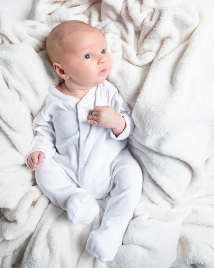 Baby Photography East Grinstead West Sussex a litlte boy in a white baby sleepsuit against a white blanket backdrop