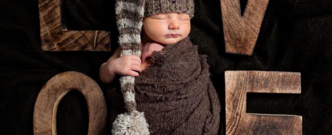 a newborn wrapped in a brown swadding sleeps surrounding by letters that spell love