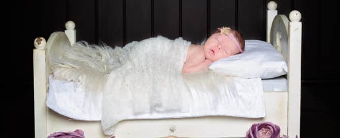 a newborn girl sleeps on a mini white bed with lilac florals