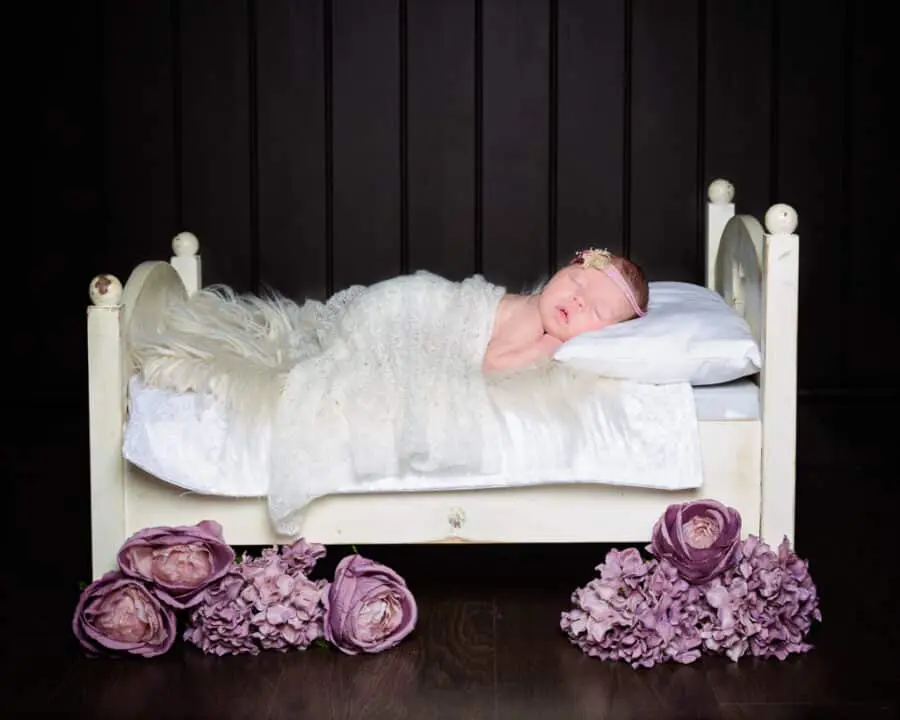 a newborn girl sleeps on a mini white bed with lilac florals