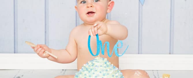 a baby sits behind a giant blue cupcake against a blue background at a first birthday photoshoot