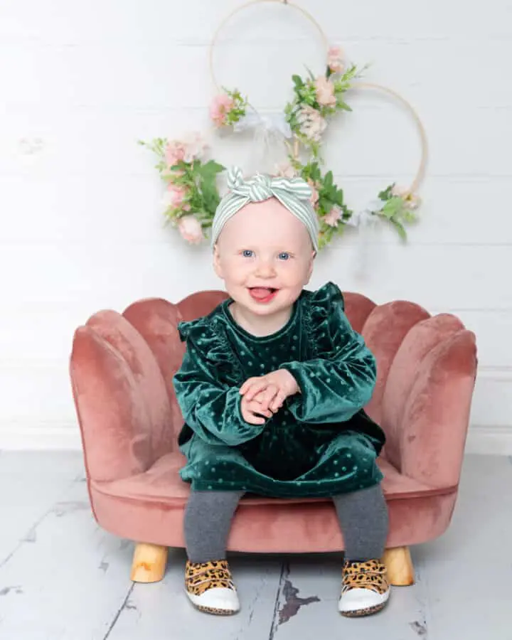 a little girl in a green dress on a pink chair in front of a flower hoop