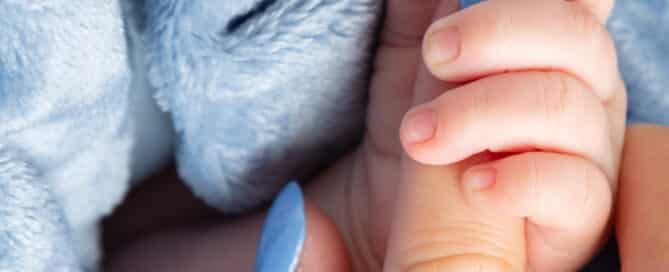 a tiny hand holds their mums finger against a blue background