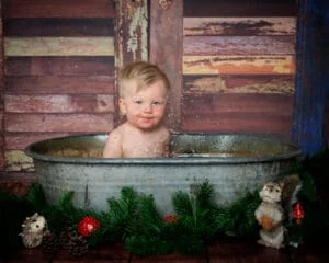 a little boy splashes in a rustic tin tub with woodland creature props around him at his first birthday photo shoot