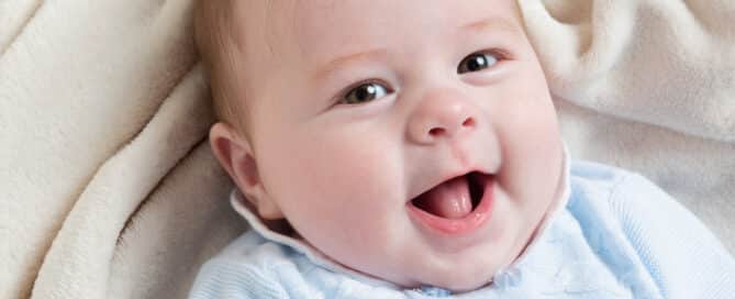 a little boy is lying on a cream blanket, looking up at the camera and smiling