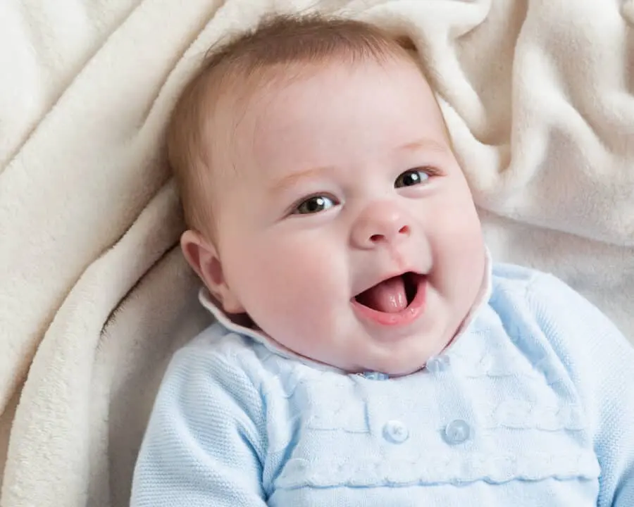 a little boy is lying on a cream blanket, looking up at the camera and smiling